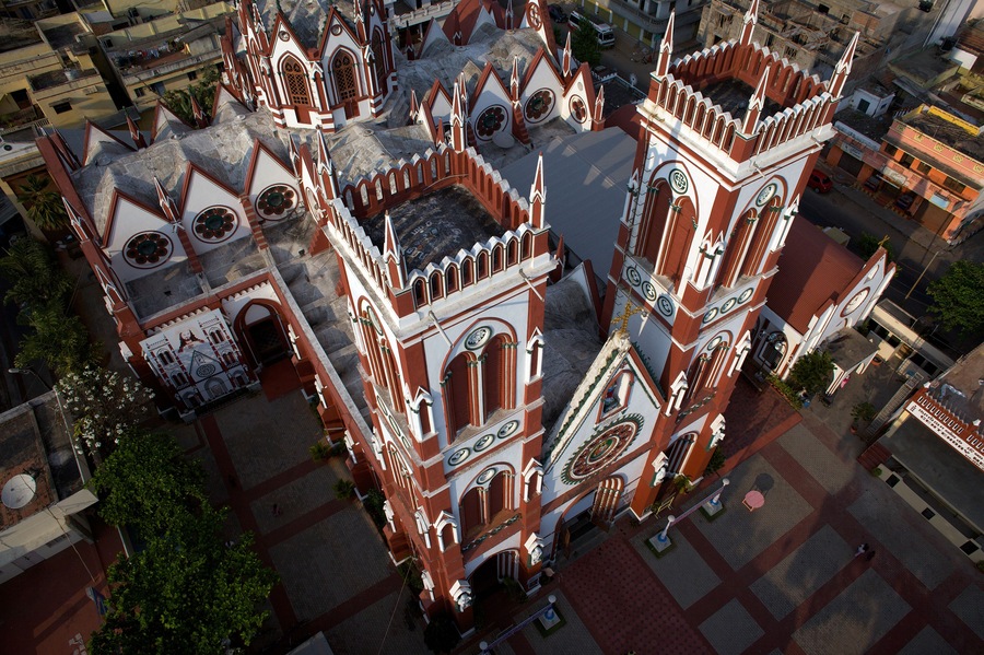 Aerial view of the red and white spires of the Poondi Madha Basilica rise majestically against the earth-toned cityscape, Tamil Nadu, India.