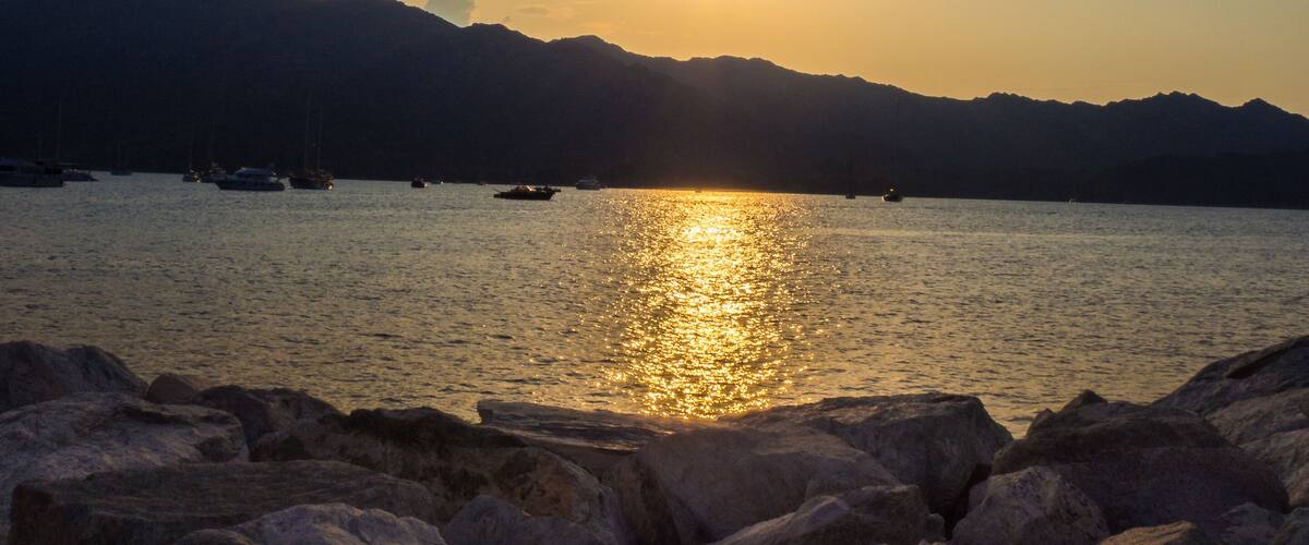 A sunset over a calm sea with rocky shores and distant mountains.
