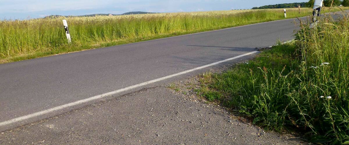 A rural road with a grassy field on one side and a clear sky.