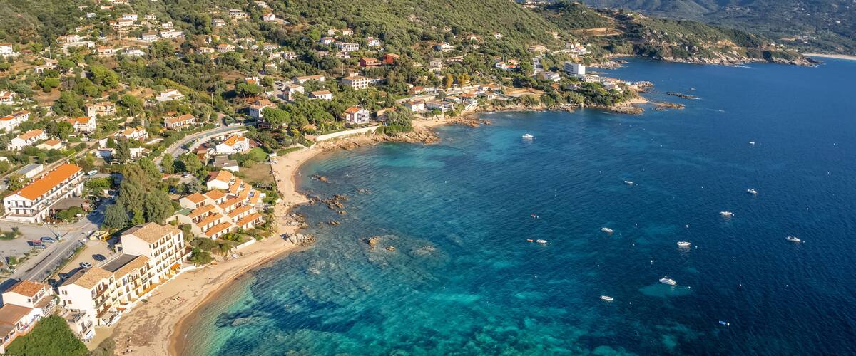 A coastal town with buildings on a hillside, a beach, and clear blue waters.