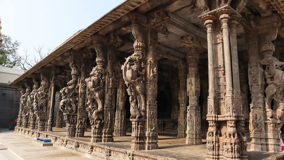 Intricately carved stone pillars with mythological figures and a temple roof structure.