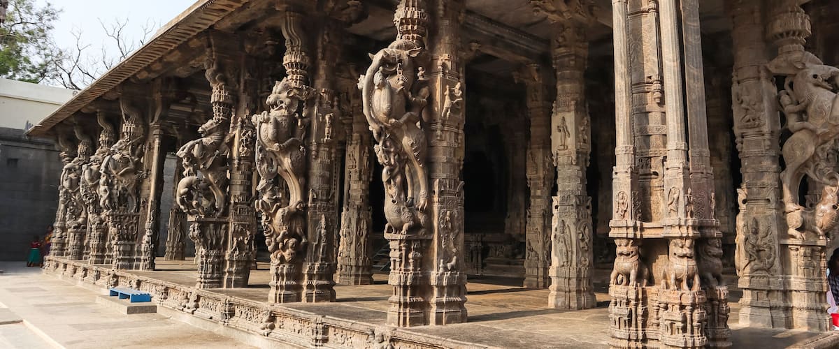 Intricately carved stone pillars with mythological figures and a temple roof structure.