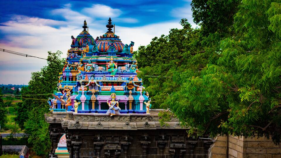 A colorful temple with intricate carvings and statues, surrounded by lush greenery.