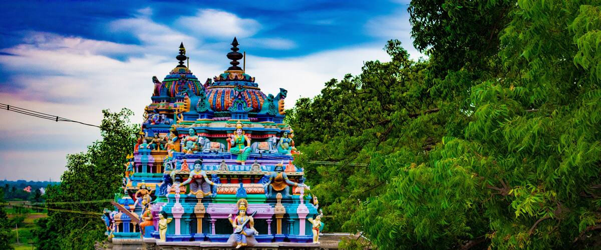 A colorful temple with intricate carvings and statues, surrounded by lush greenery.