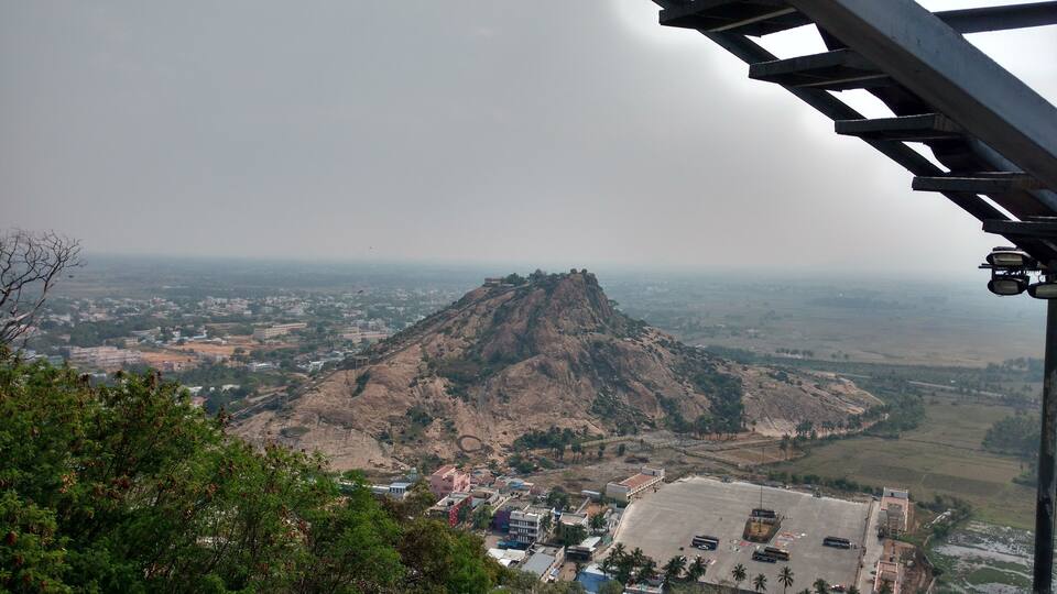 A mountain with a temple on top, surrounded by buildings and greenery.