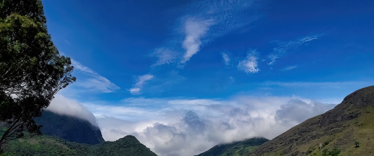 A mountainous landscape with a river, dense greenery, and a clear sky with clouds.