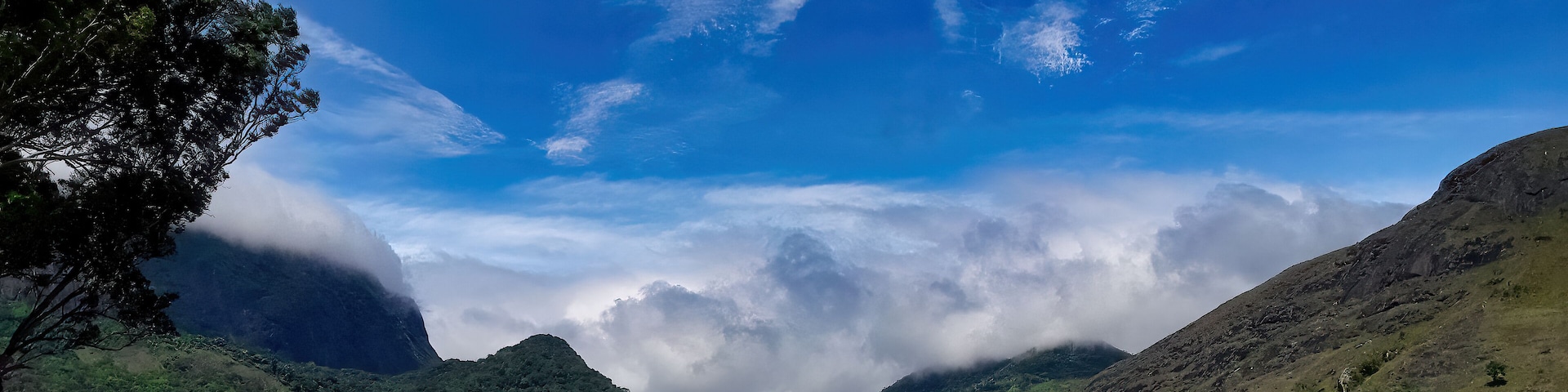 A mountainous landscape with a river, dense greenery, and a clear sky with clouds.