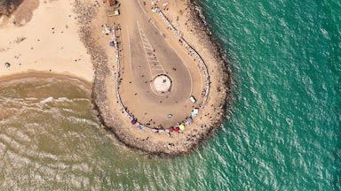 An aerial view of a beach with a circular stone structure surrounded by umbrellas and people.