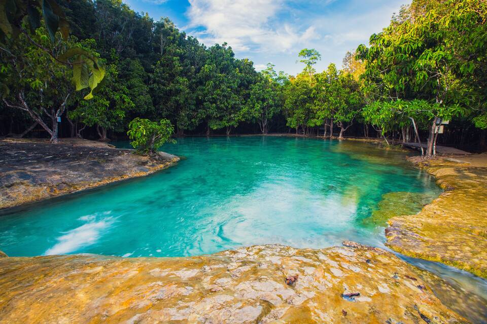 A turquoise river surrounded by dense green foliage and rocky terrain.