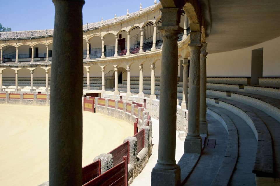 Um antigo anfiteatro romano com arcos de pedra e uma arena de areia.