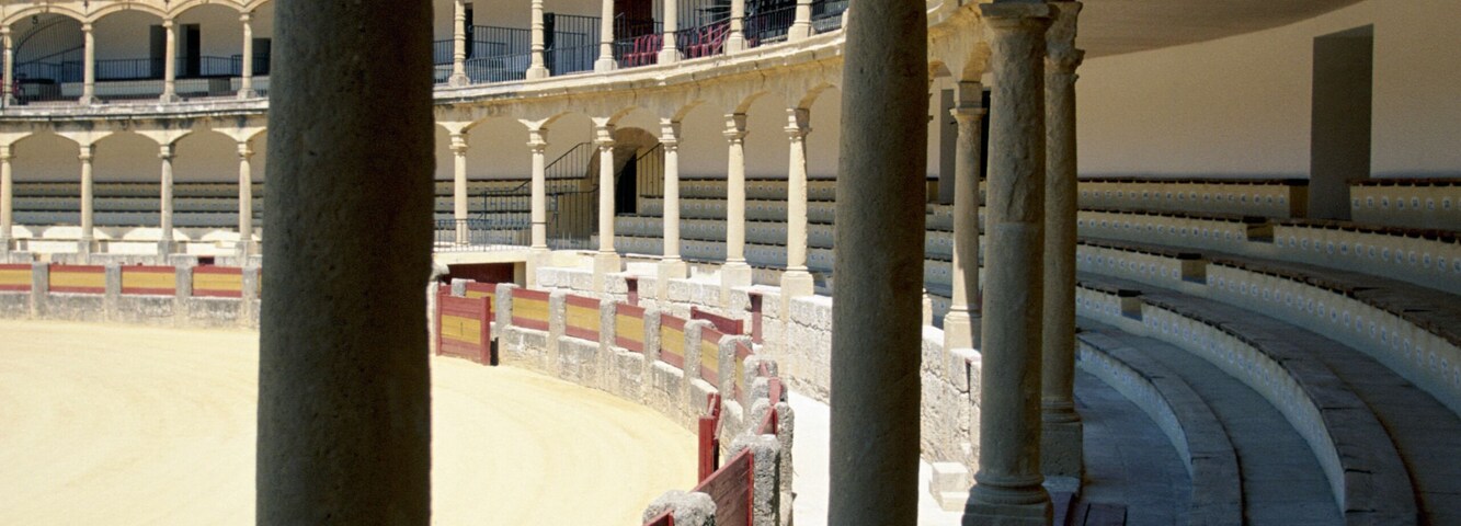 Um antigo anfiteatro romano com arcos de pedra e uma arena de areia.