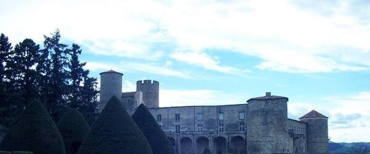 A castle with a long driveway, a stone wall, and a tower.