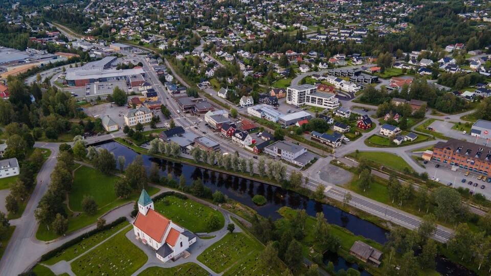 An aerial view of a town with a church, a river, and surrounding greenery.