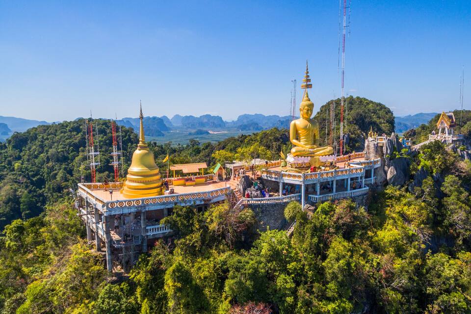 A large golden statue on a mountain with a temple complex.