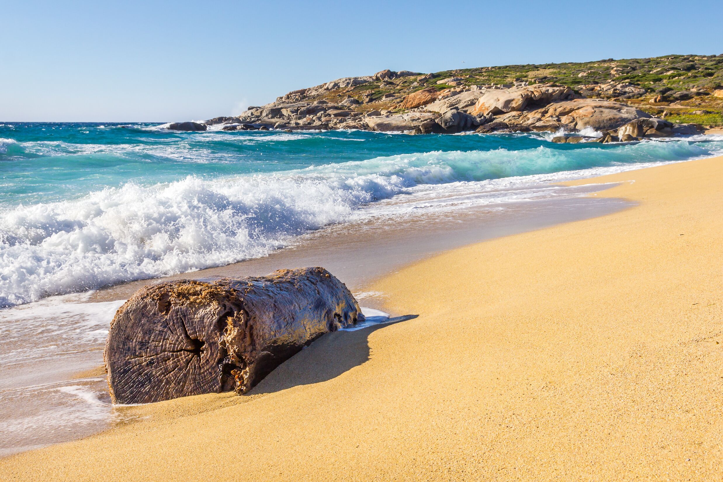 A sandy beach with waves, a large rock, and a rocky coastline.