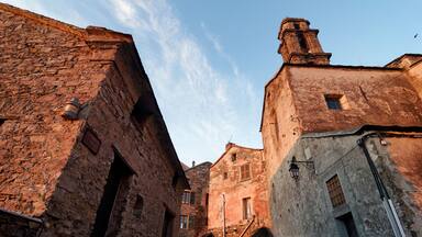 A narrow street with old stone buildings, a clear sky, and a bird flying.
