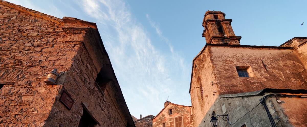 A narrow street with old stone buildings, a clear sky, and a bird flying.