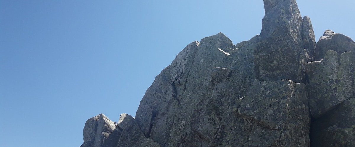 A rugged mountain peak with sharp, jagged edges and a clear blue sky in the background.