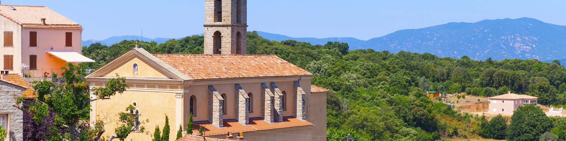 Eine Kirche mit einem Glockenturm, umgeben von üppiger Vegetation und Bergen im Hintergrund.