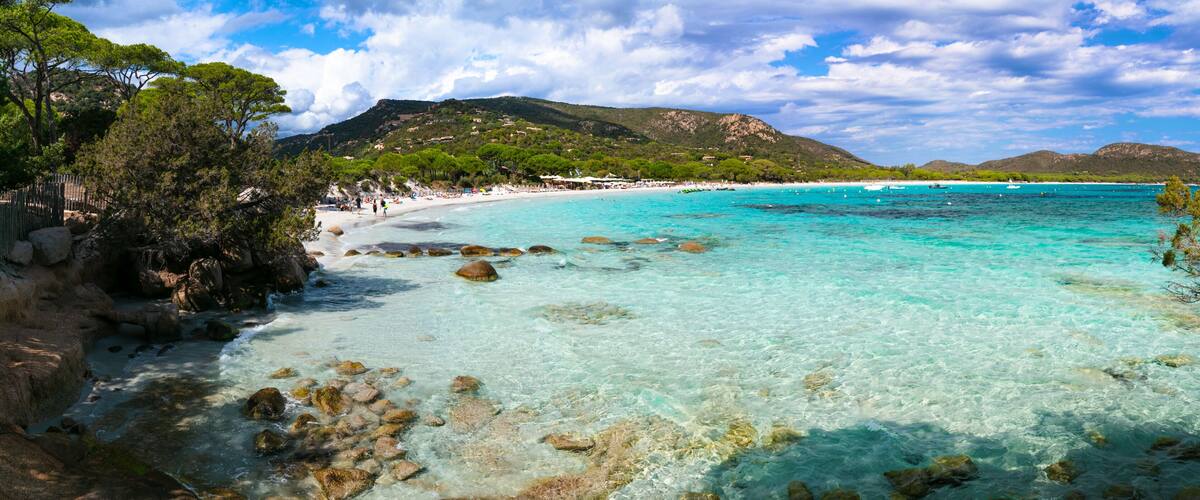 A coastal landscape with clear turquoise waters, rocky shorelines, and a backdrop of green hills.