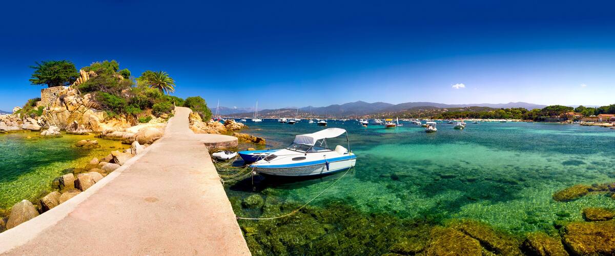 A coastal path leading to a rocky island with boats in the water.