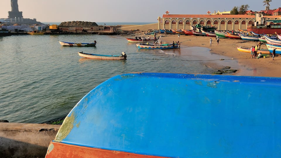 A coastal scene with boats, a statue, and a building with arches.