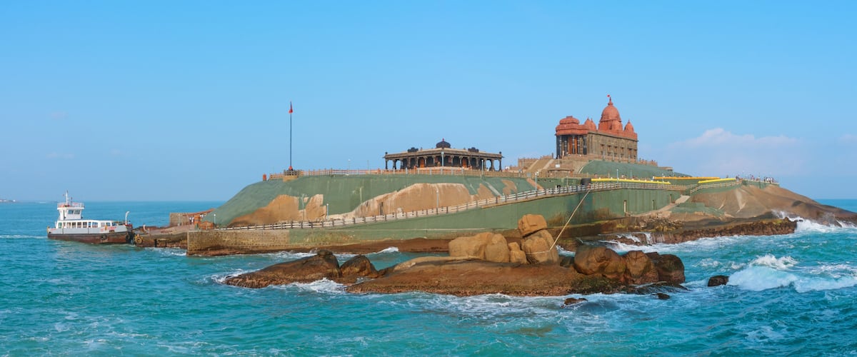 A coastal fortress with a prominent red-roofed building and a smaller structure on a rocky outcrop.