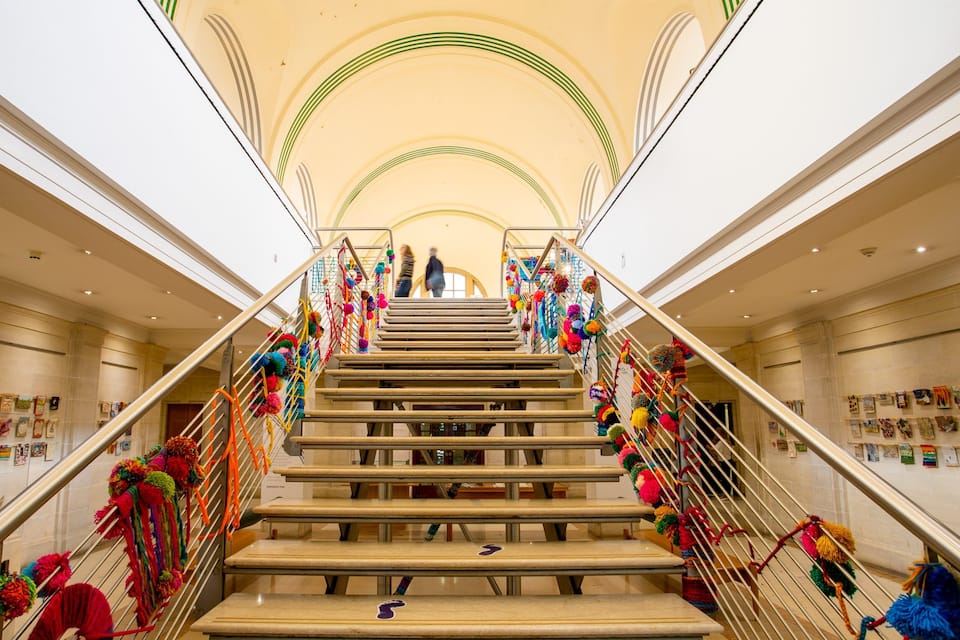A grand staircase with colorful pom-poms and artwork on the walls.
