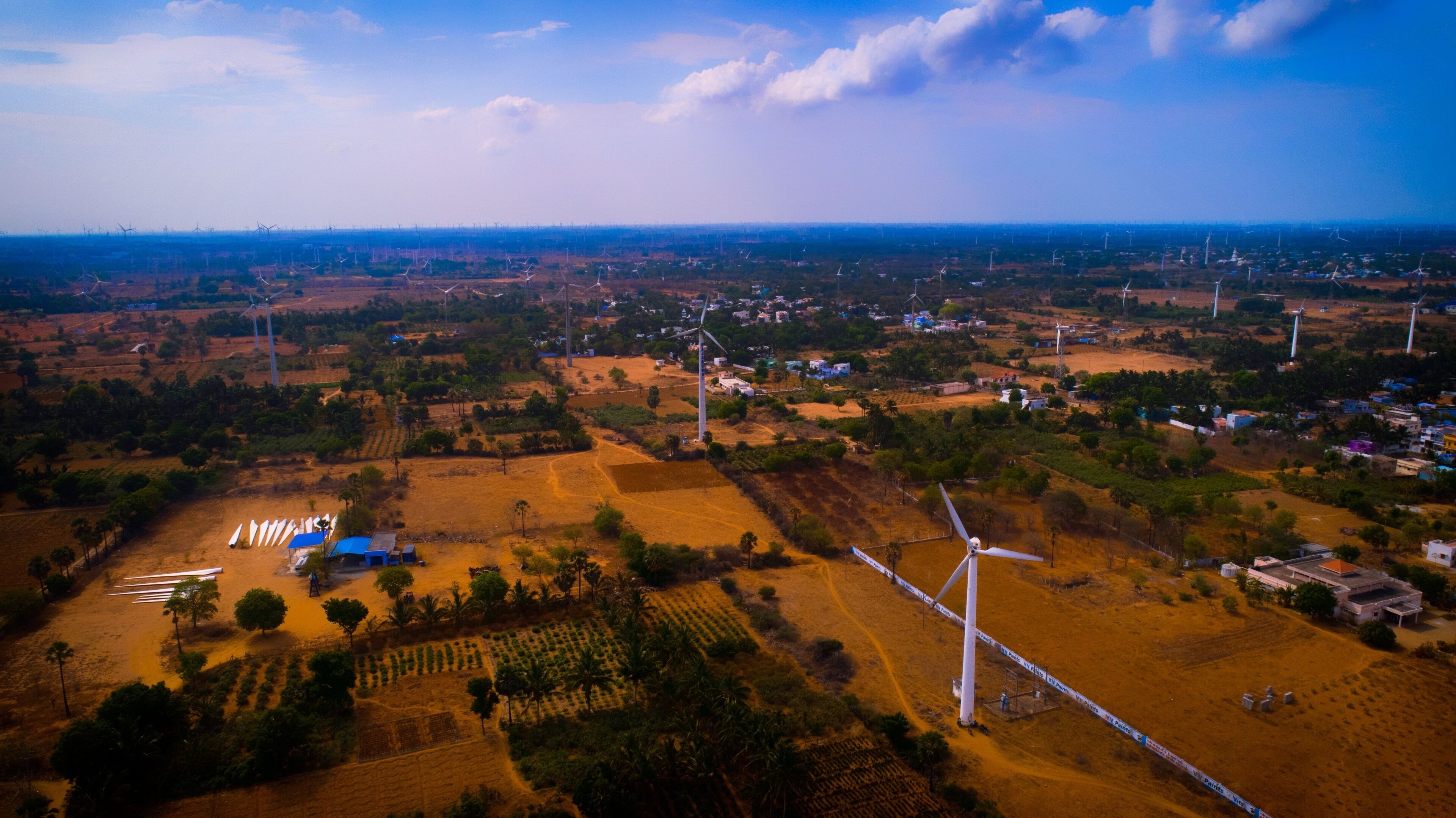 An aerial view of a rural landscape with wind turbines, fields, and scattered buildings.