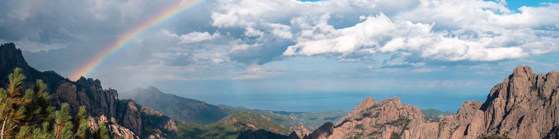 A mountain landscape with a rainbow, dense forests, and rocky outcrops.