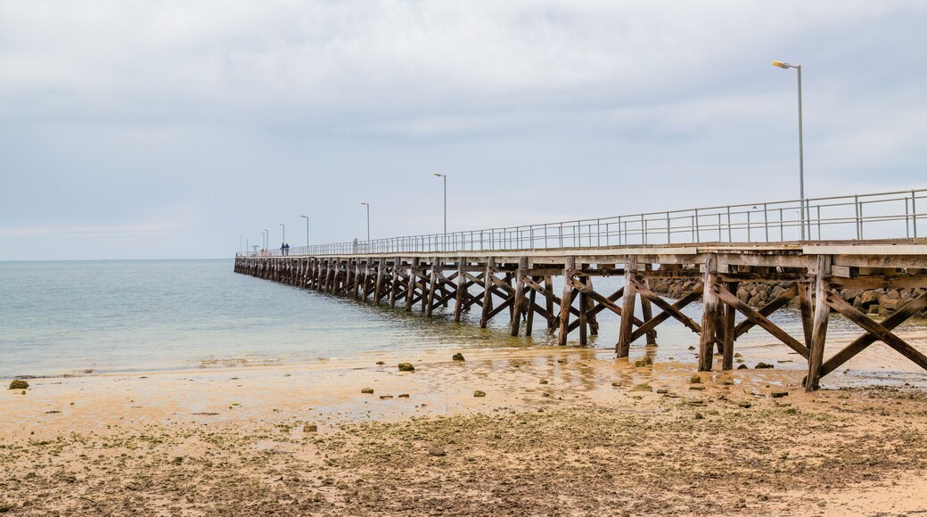 An old wooden jetty at low tide with calm sea and a stony beach under an overcast sky and the jetty is used for fishing, at Stansbury on the Yorke Peninsula in South Australia.