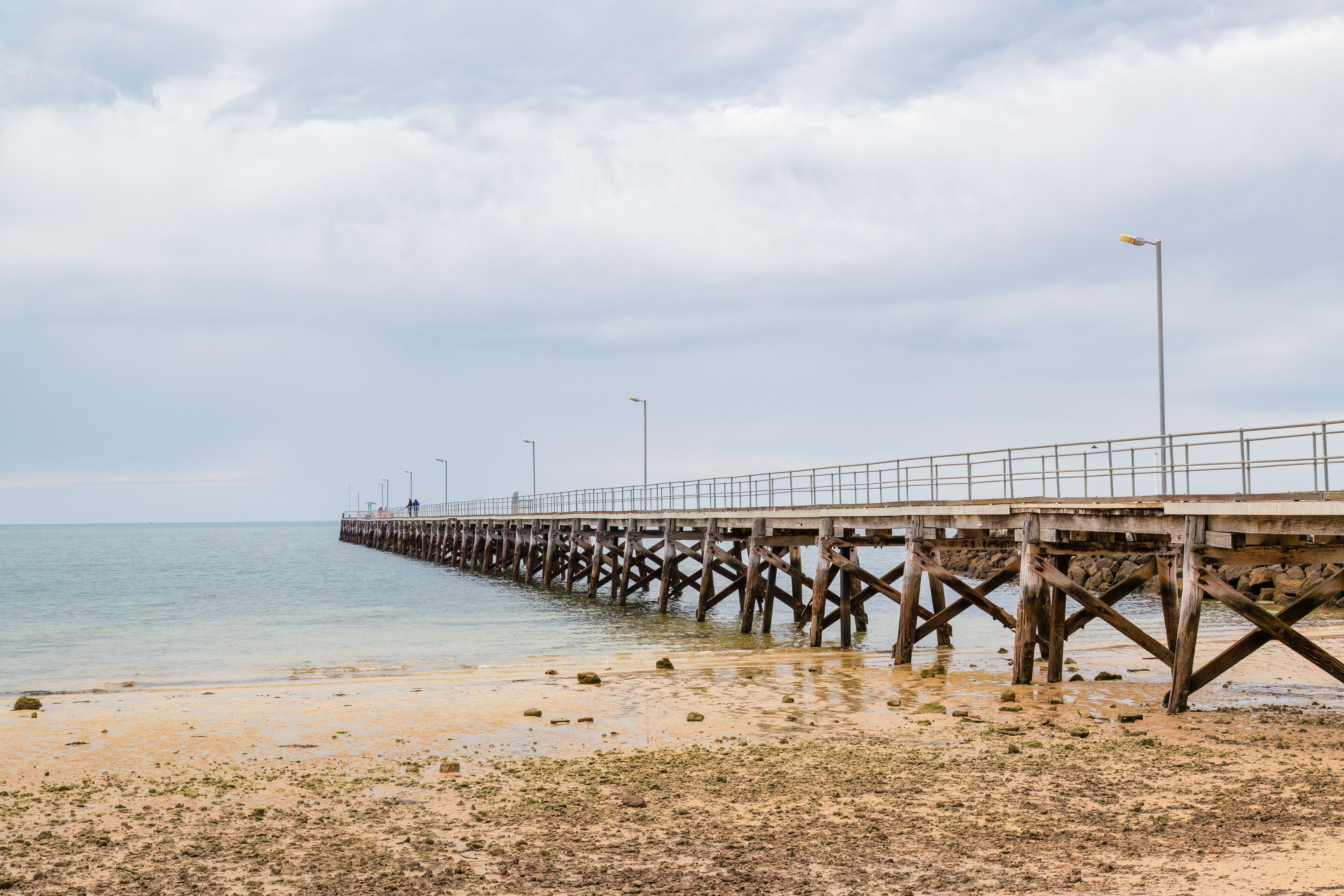 A wooden pier extending into calm waters, with a sandy beach in the foreground.