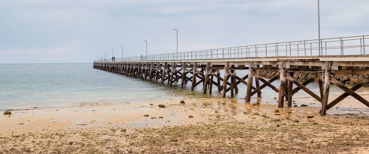 A wooden pier extending into calm waters, with a sandy beach in the foreground.