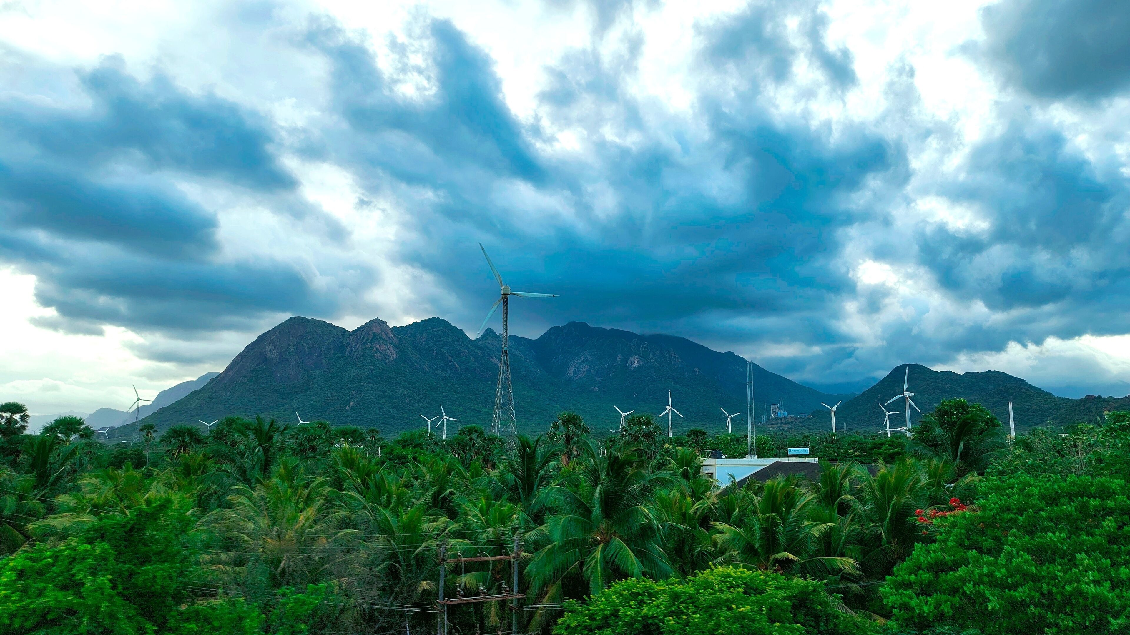 Scenic view en route to Kanyakumari from Aralvaimozhi, featuring lush greenery, towering windmills, and the backdrop of dramatic mountains under a cloudy sky.