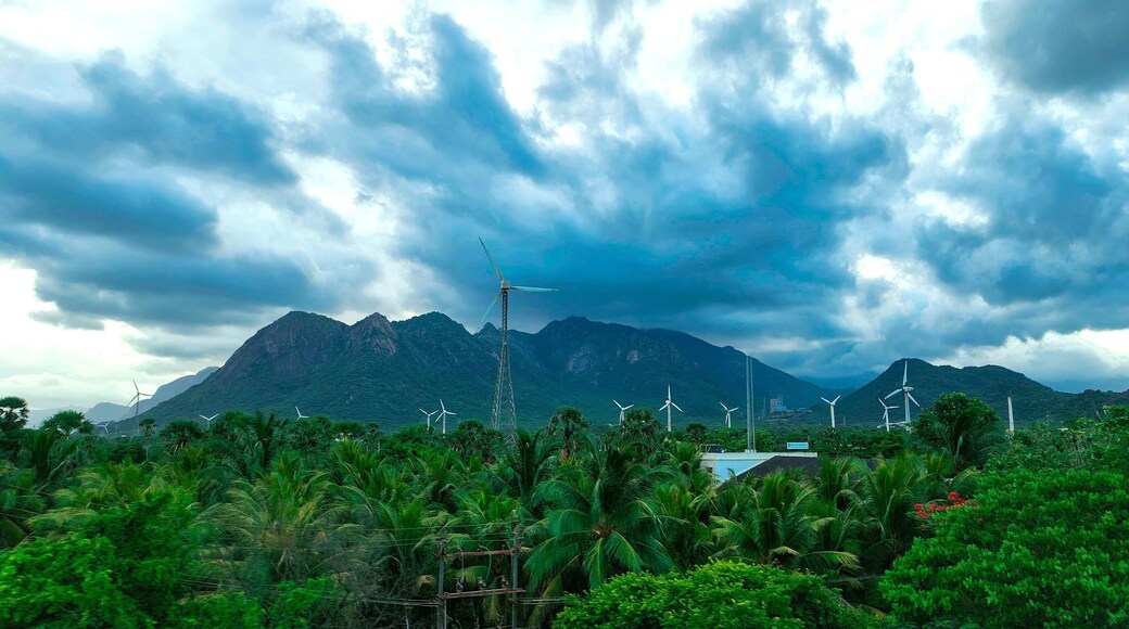 Scenic view en route to Kanyakumari from Aralvaimozhi, featuring lush greenery, towering windmills, and the backdrop of dramatic mountains under a cloudy sky.