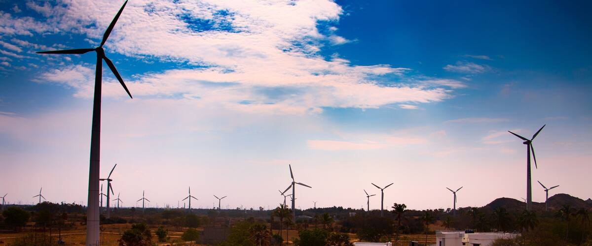 A wind farm with multiple wind turbines in a rural landscape with sparse vegetation and a few buildings.