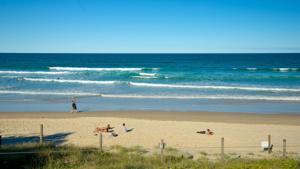 Ein Strand mit Wellen, badenden Personen und blauem Himmel.