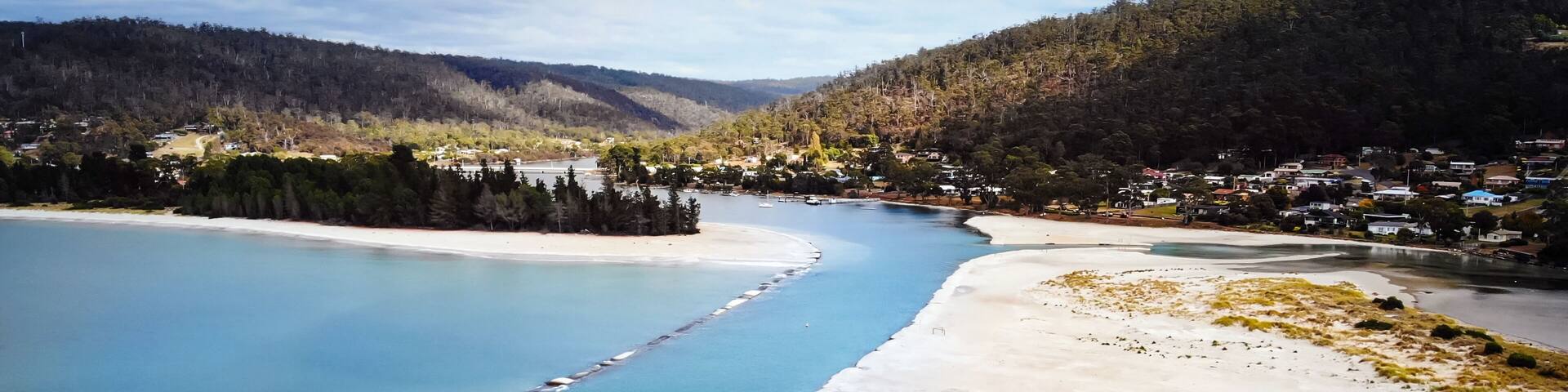 A coastal landscape with a river, a sandy beach, and a forested hill.