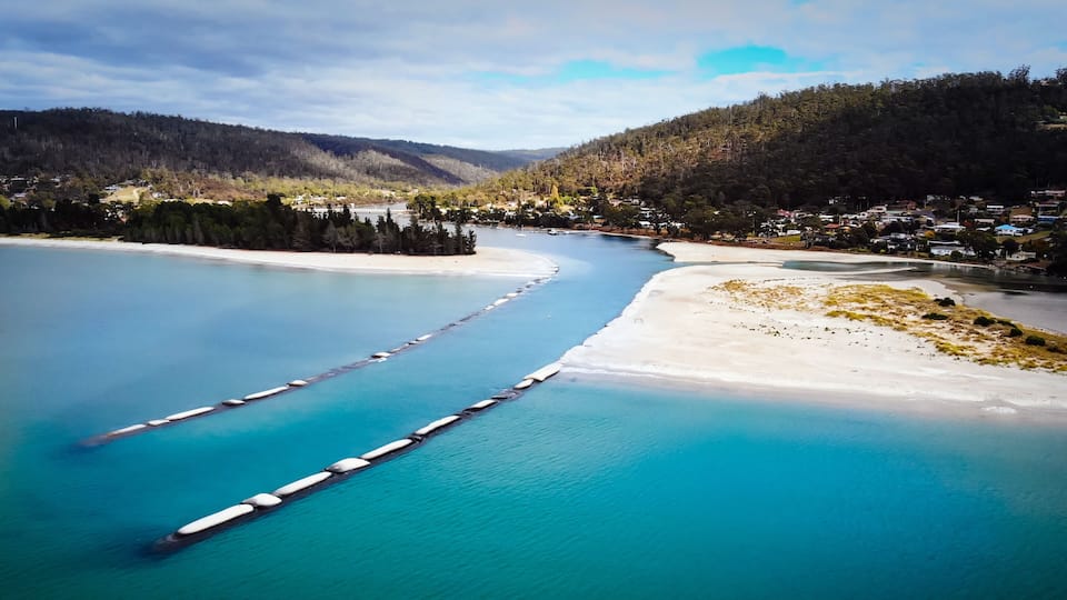 A coastal landscape with a river, a sandy beach, and a forested hill.