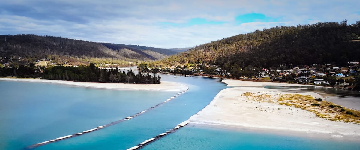 A coastal landscape with a river, a sandy beach, and a forested hill.
