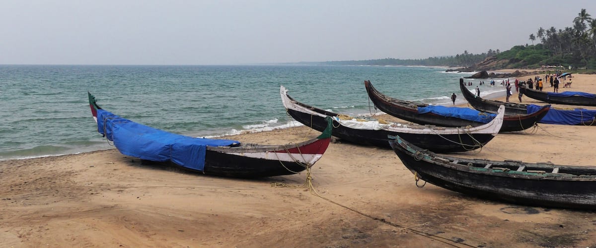 Several traditional boats tied to a sandy beach with the ocean in the background.
