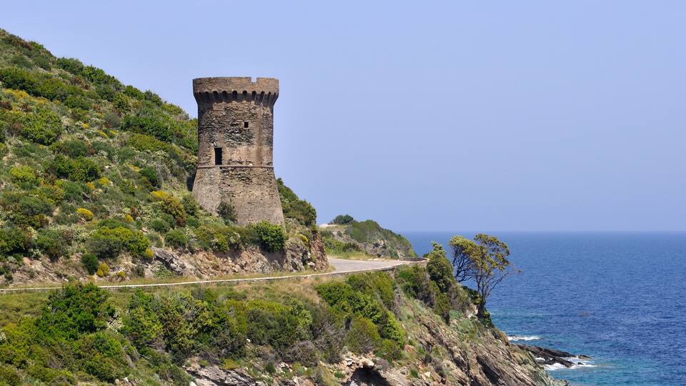A coastal tower on a hillside with a road leading to it.