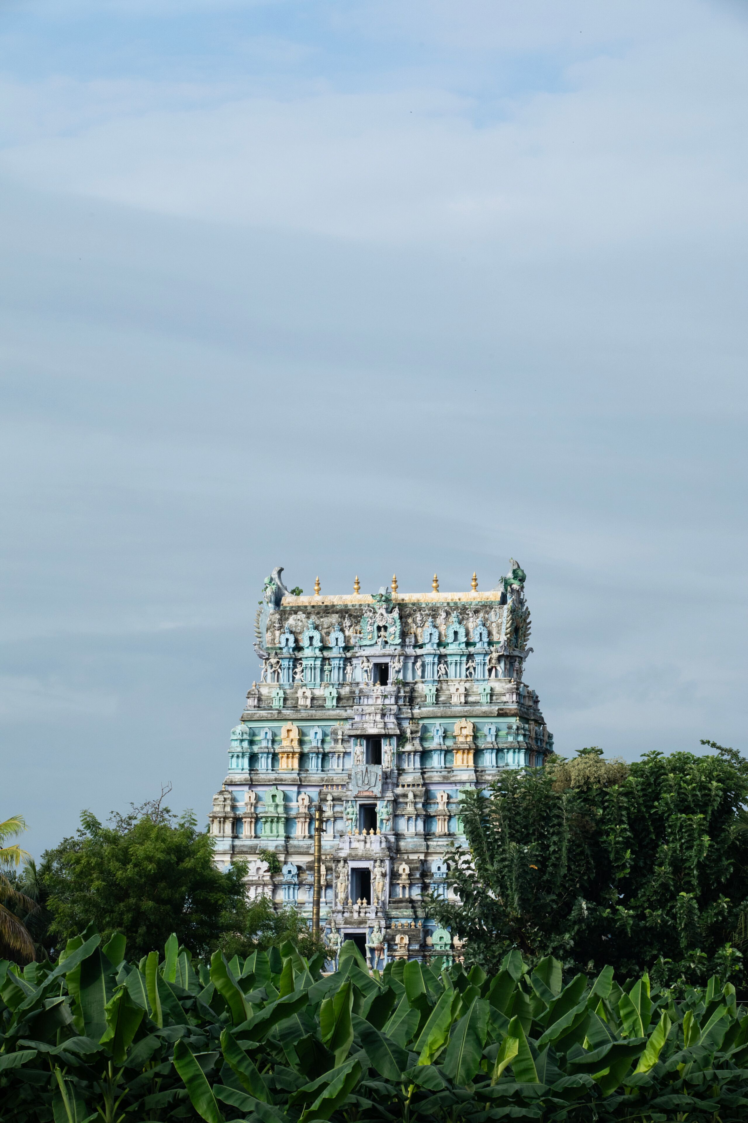 A multi-tiered temple with intricate carvings and a blue and gold color scheme, surrounded by lush greenery.