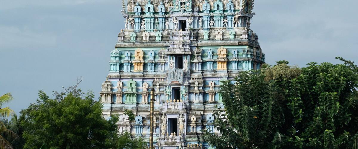 A multi-tiered temple with intricate carvings and a blue and gold color scheme, surrounded by lush greenery.