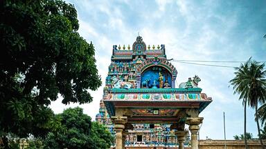 A temple with intricate carvings and statues, surrounded by trees and a paved walkway.