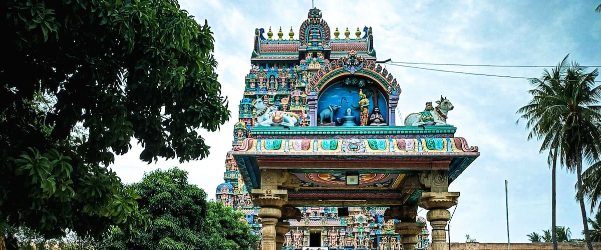 A temple with intricate carvings and statues, surrounded by trees and a paved walkway.