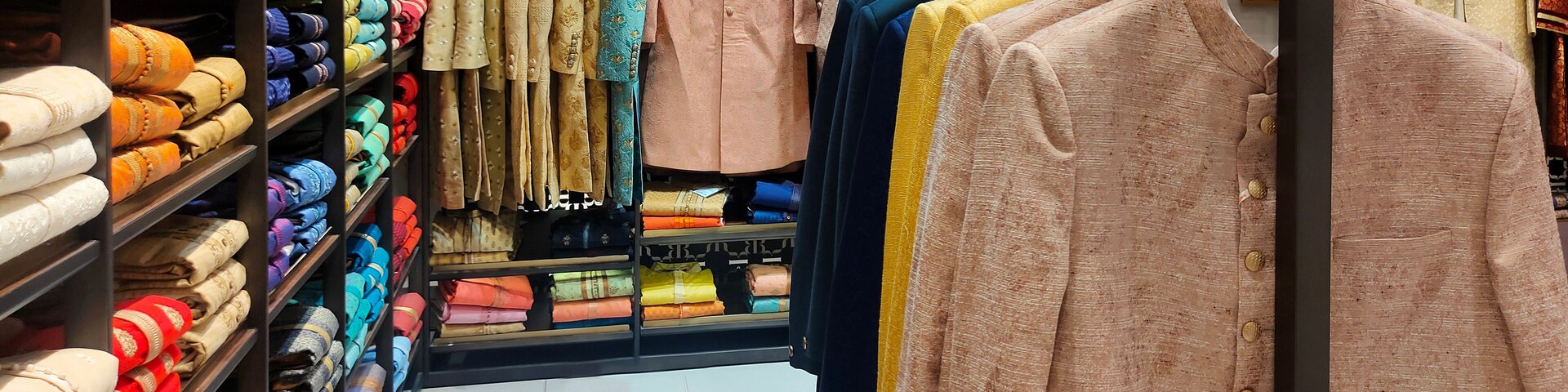 A clothing store with shelves of folded fabrics and racks of garments.