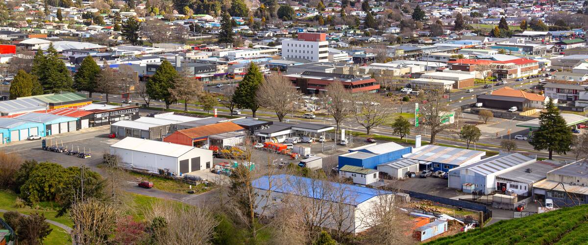 A town with industrial buildings, roads, and green hills in the background.