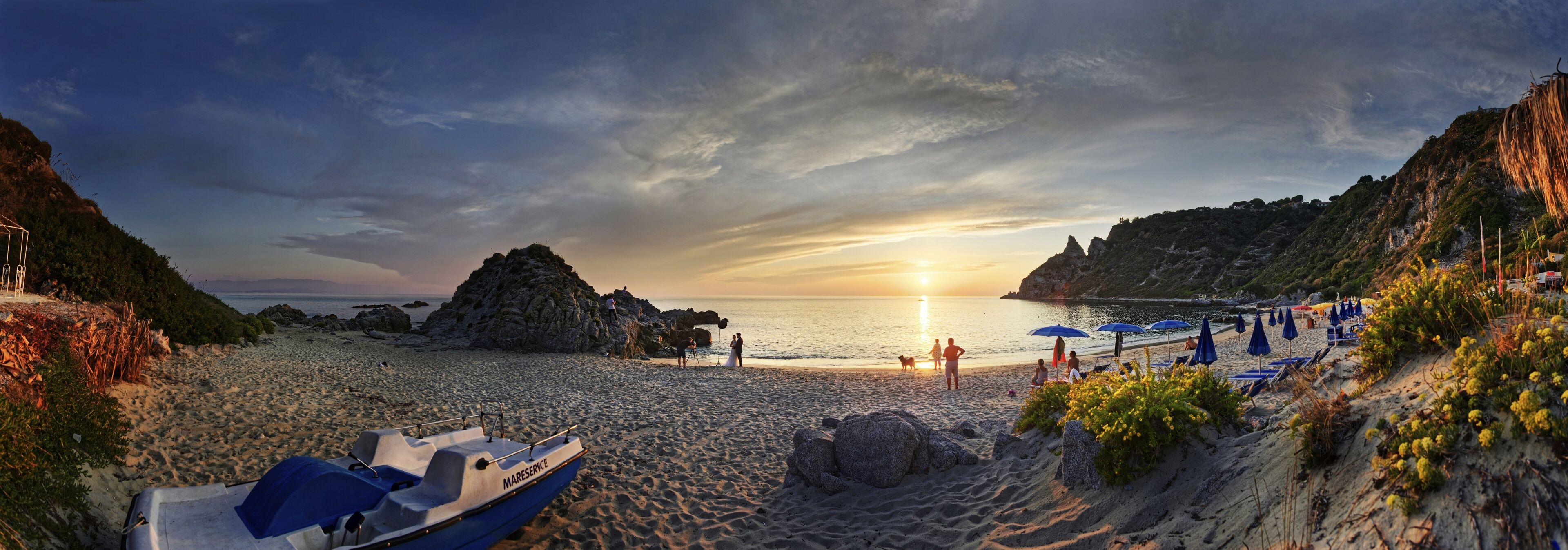 A beach with a boat, rocky cliffs, and umbrellas.