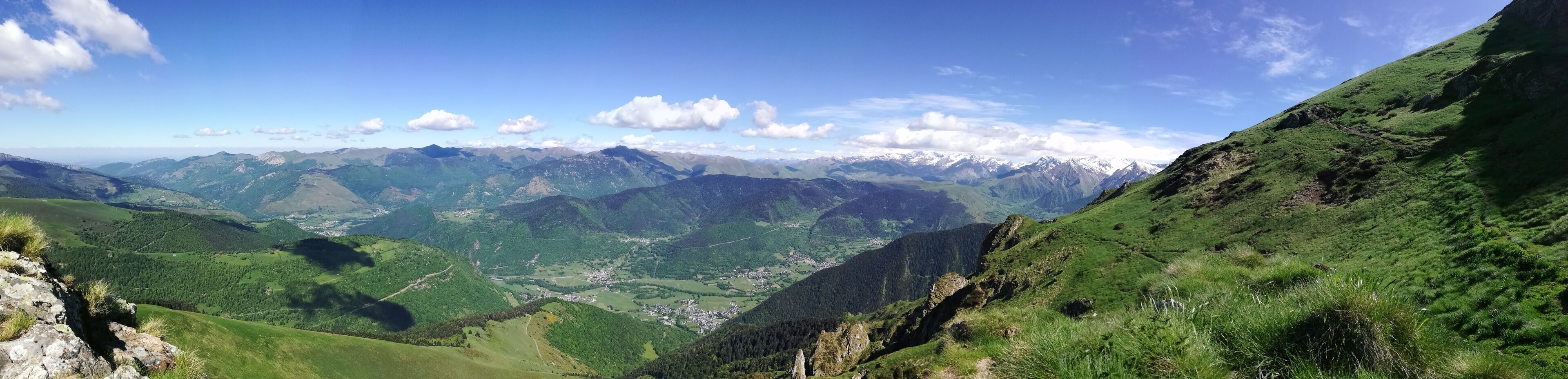 A mountainous landscape with green valleys and distant snow-capped peaks under a clear sky.